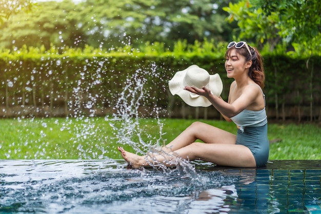 スイミングプールの端に座って水しぶきを遊んでいる若い女性