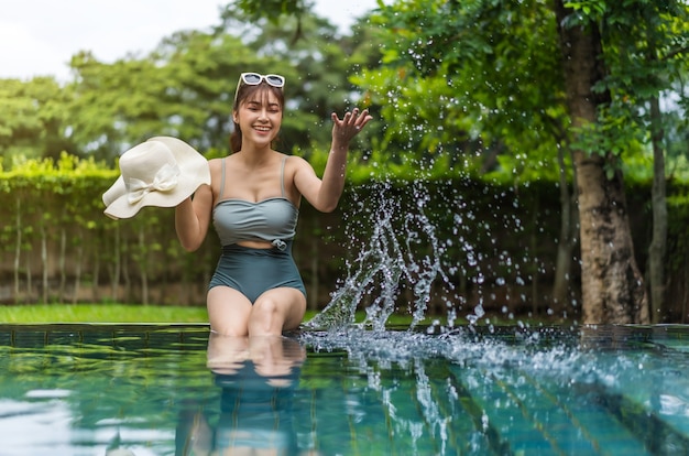 Молодая женщина сидит на краю бассейна и играет с брызгами воды