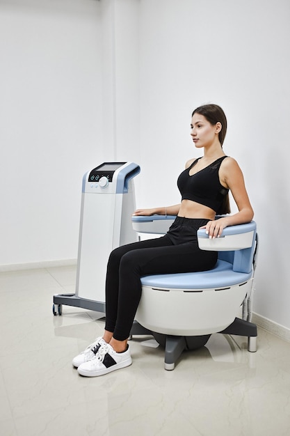 Молодая женщина сидит на электромагнитном стуле для стимуляции глубоких мышц тазового дна и восстановления нервно-мышечного контроля в клинике