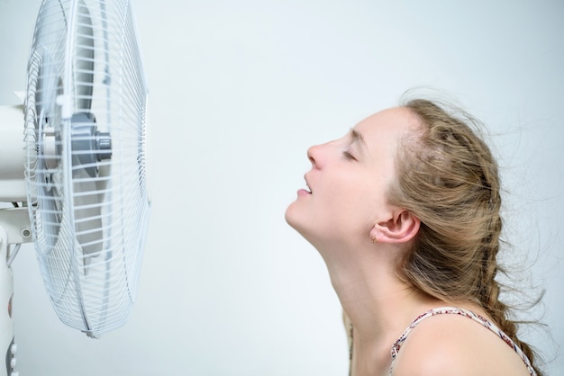 Foto giovane donna che si siede sotto un fan con gli occhi chiusi da piacere. caldo estivo.