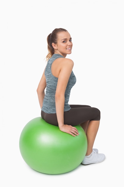 Young woman sitting on fitness ball looking over shoulder at camera