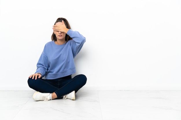 Photo young woman sitting on the floor covering eyes by hands. do not want to see something