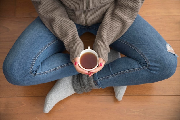 一杯のコーヒーを楽しんで床に座っている若い女性