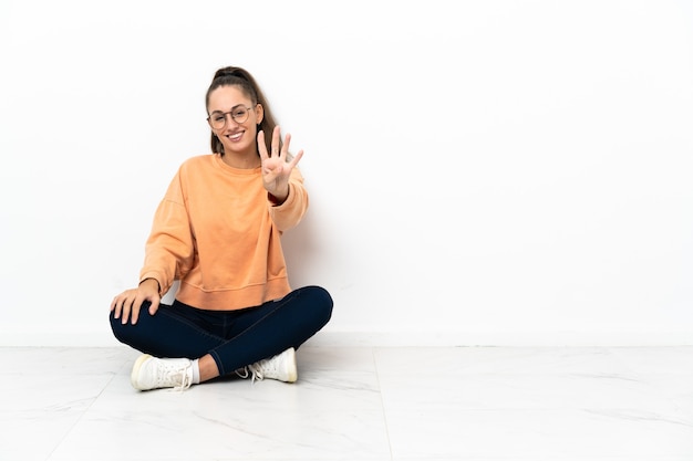 Photo young woman sitting on the floor happy and counting four with fingers