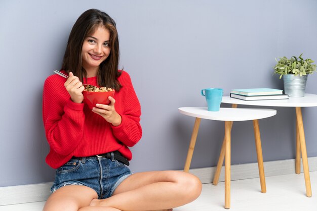 床に座って、穀物のボウルを保持している若い女性