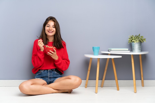 Young woman sitting on the floor and holding a bowl of cereals