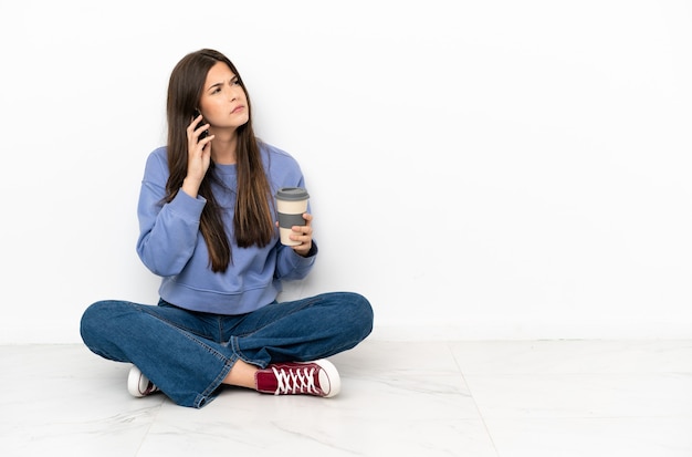 Young woman sitting on the floor holding coffee to take away and a mobile