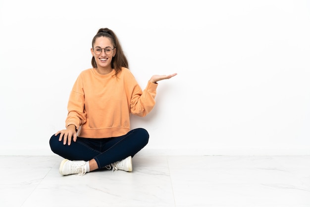 Young woman sitting on the floor holding copyspace imaginary on the palm to insert an ad