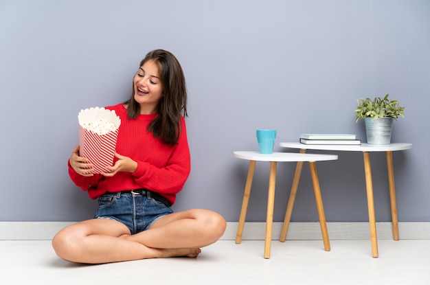 Young woman sitting on the floor and holding popcorns