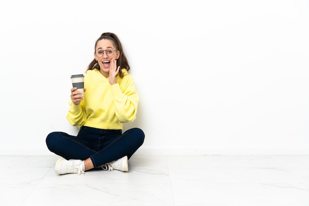 Young woman sitting on the floor holding a take away coffee shouting with mouth wide open