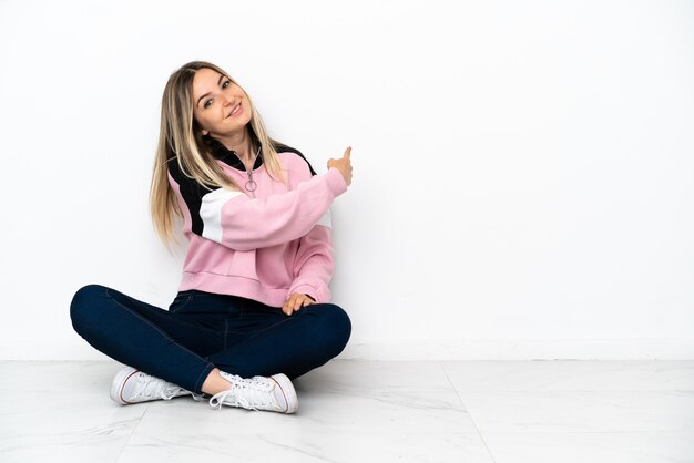 Young woman sitting on the floor at indoors pointing back