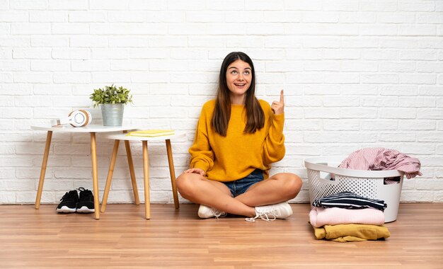 洋服バスケットを上に向けて驚いて屋内で床に座っている若い女性