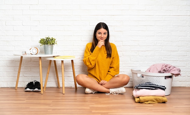 Young woman sitting on the floor at indoors with clothes basket thinking