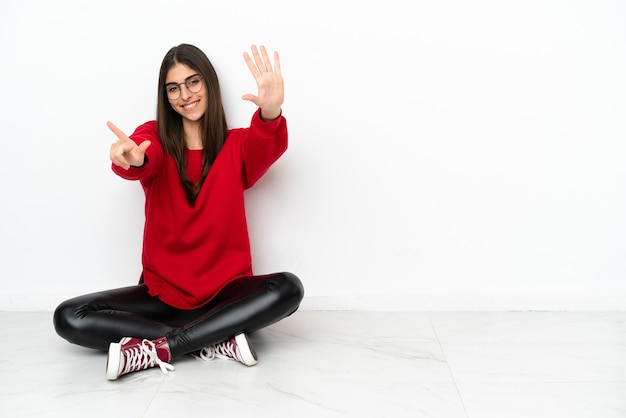 Young woman sitting on the floor isolated on white background counting seven with fingers