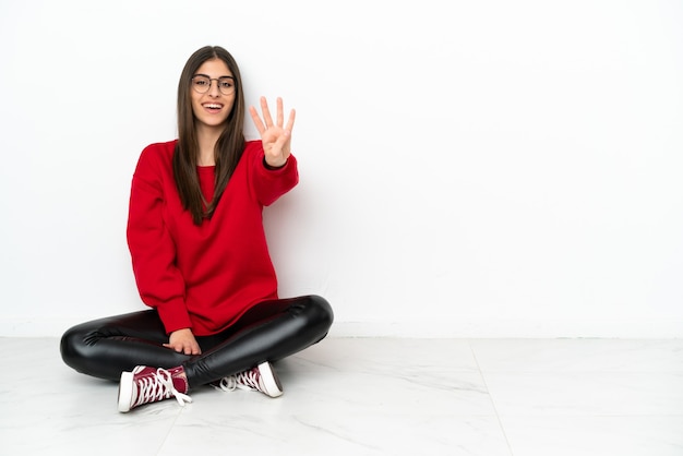 Young woman sitting on the floor isolated on white background happy and counting four with fingers