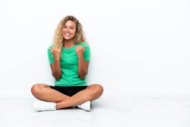 Young woman sitting on the floor isolated on white background happy and smiling