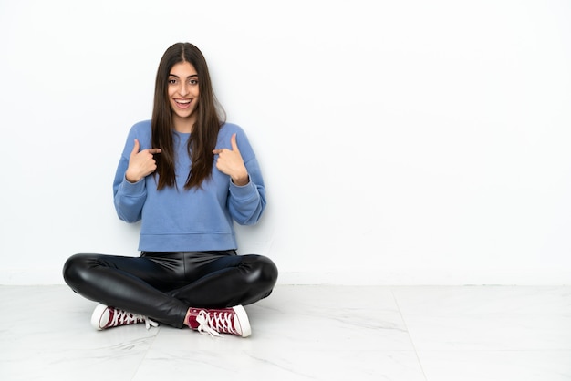 Young woman sitting on the floor isolated on white background with surprise facial expression