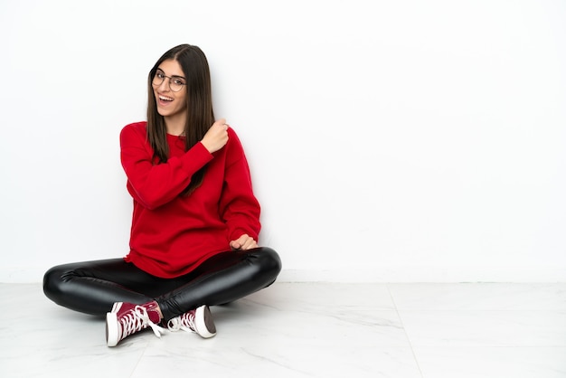 Young woman sitting on the floor isolated on white wall celebrating a victory