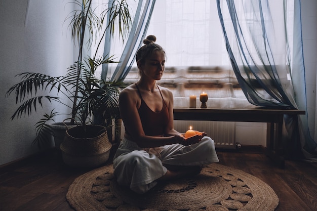 Young woman sitting on the floor lights candles enjoy meditation do yoga exercise at home mental