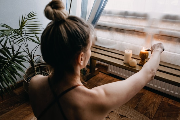 Young woman sitting on the floor lights candles enjoy meditation do yoga exercise at home mental