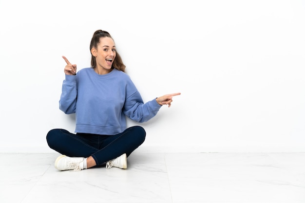 Young woman sitting on the floor pointing finger to the laterals and happy