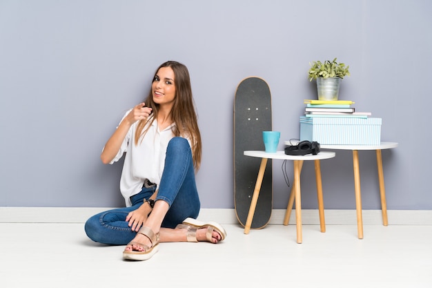 Young woman sitting on the floor points finger at you