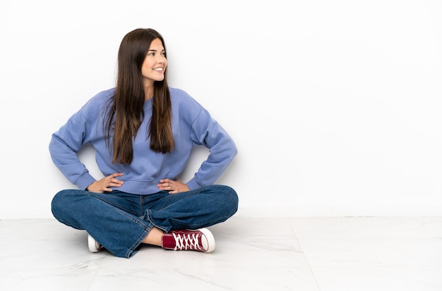 Young woman sitting on the floor posing with arms at hip and smiling