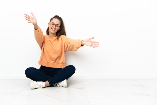 Young woman sitting on the floor presenting and inviting to come with hand