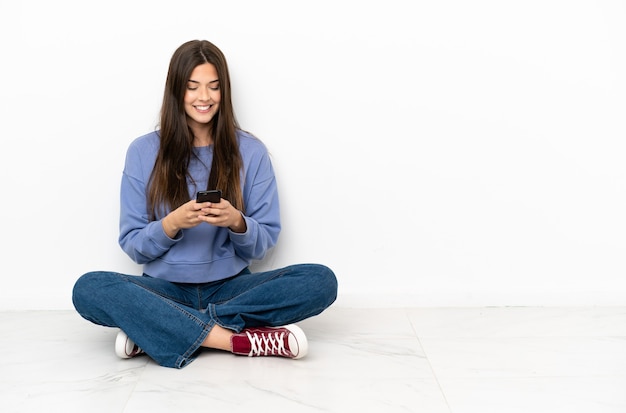 Молодая женщина сидит на полу, отправляя сообщение с мобильного телефона