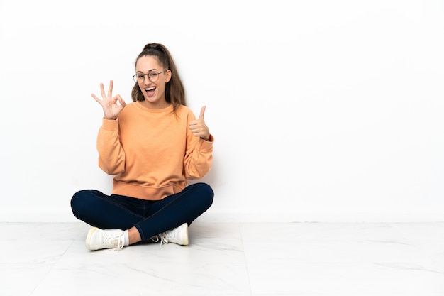Young woman sitting on the floor showing ok sign and thumb up gesture