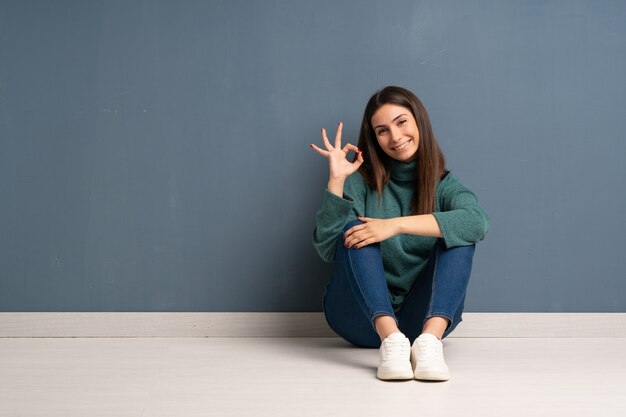 Young woman sitting on the floor showing ok sign with fingers