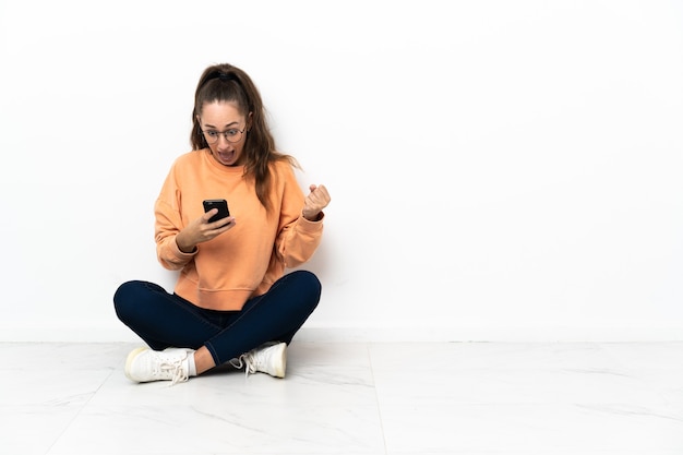 Young woman sitting on the floor surprised and sending a message