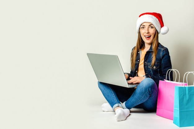 Young woman sitting on the floor and using a laptop next to shopping bags