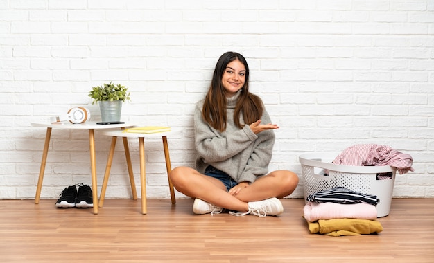 服のバスケットが付いている床の上に座っている若い女性