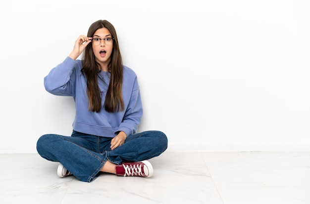 Young woman sitting on the floor with glasses and surprised