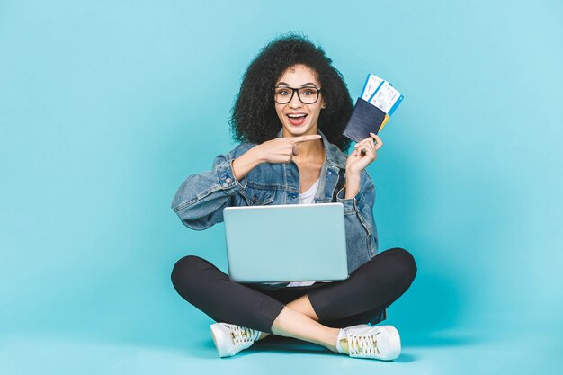 Young woman sitting on the floor with laptop and plane tickets