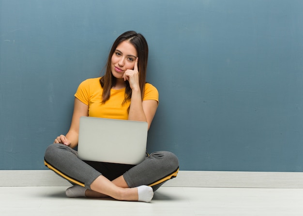Young woman sitting on the floor with a laptop thinking about an idea