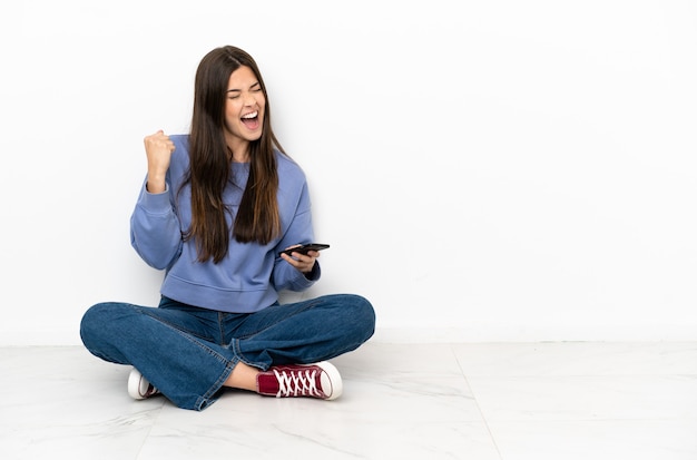 Young woman sitting on the floor with phone in victory position