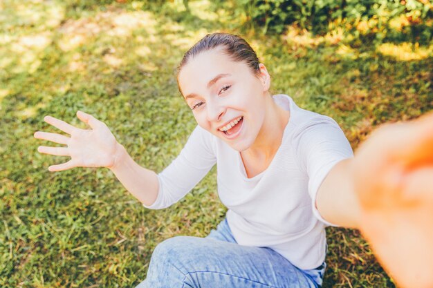 Foto giovane donna che si siede sull'erba verde e che prende i selfie