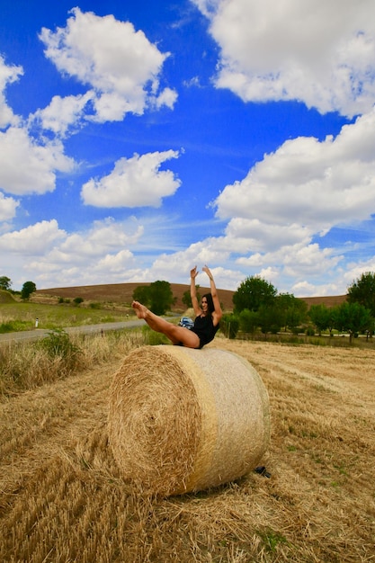 Foto giovane donna seduta su una palla di fieno in un campo agricolo