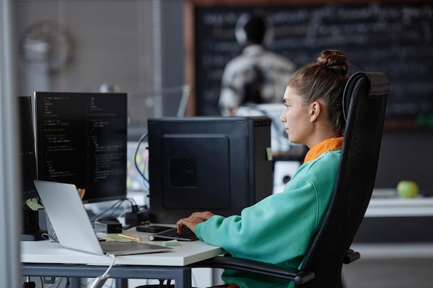 職場でコンピューターモニターの前に座り、新しいソフトウェアを開発している若い女性
