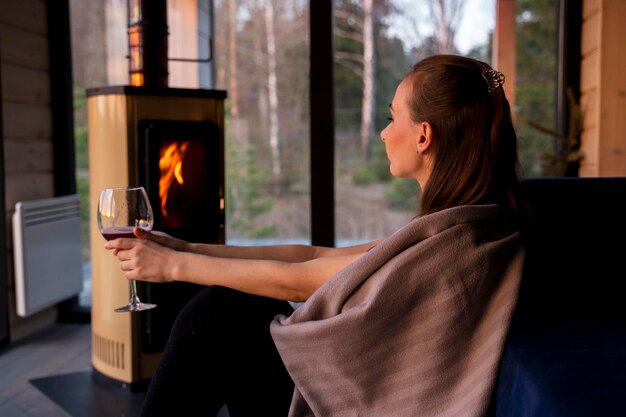家で暖炉のそばに座って赤ワインを飲んでいる若い女性
