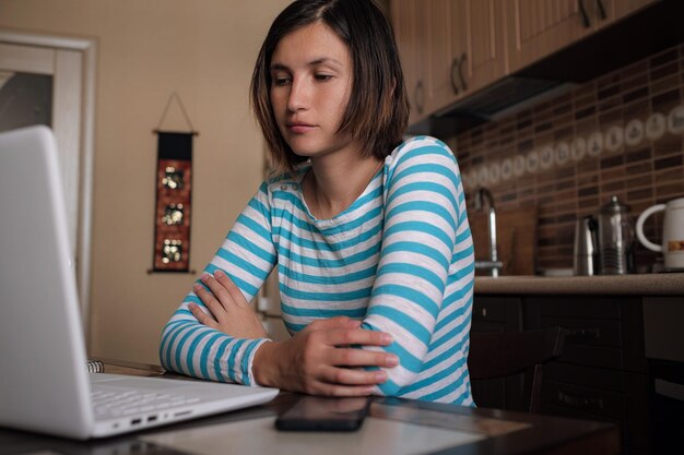 Young woman sitting in kitchen and working on laptop in morning Female using laptop dining table