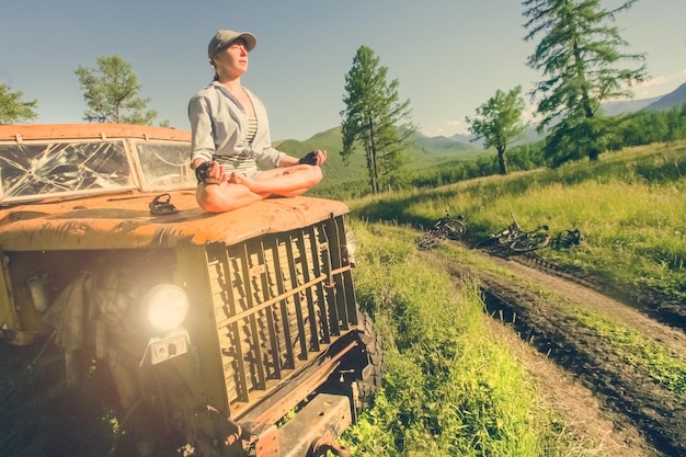 Young woman sitting in lotus position on a rusty old abandoned car