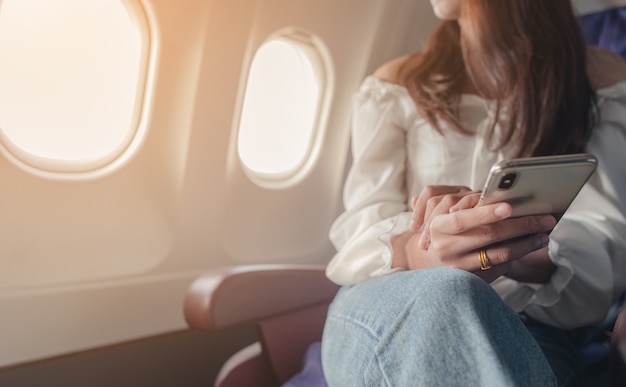 Young woman sitting near airplane window at sunset and using mobile phone during flight Airplane