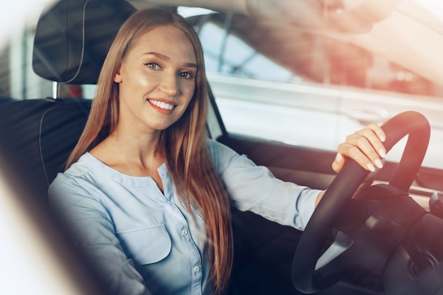 young woman sitting in new car in showroom