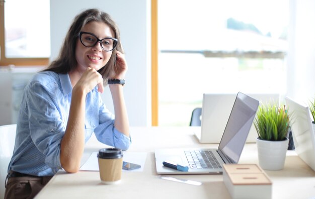 ラップトップ コンピューターの画面を見てオフィスのテーブルに座っている若い女性 若い女性