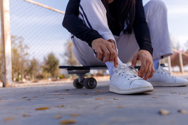 Young woman sitting on old-school skateboard tying her shoes