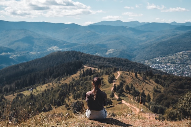Фото Молодая женщина сидит на скале с рюкзаком и смотрит на горизонт