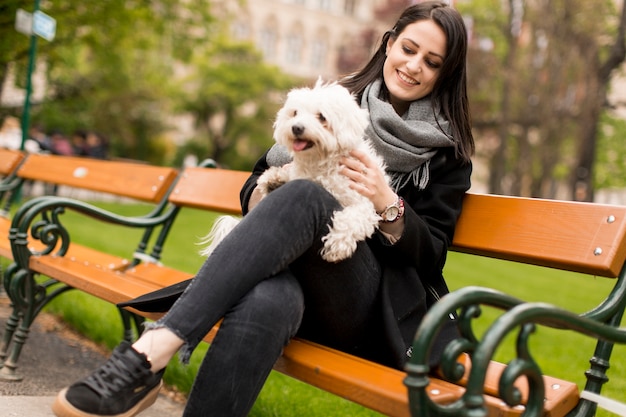 Young woman sitting in the park and holding a small dog in her lap